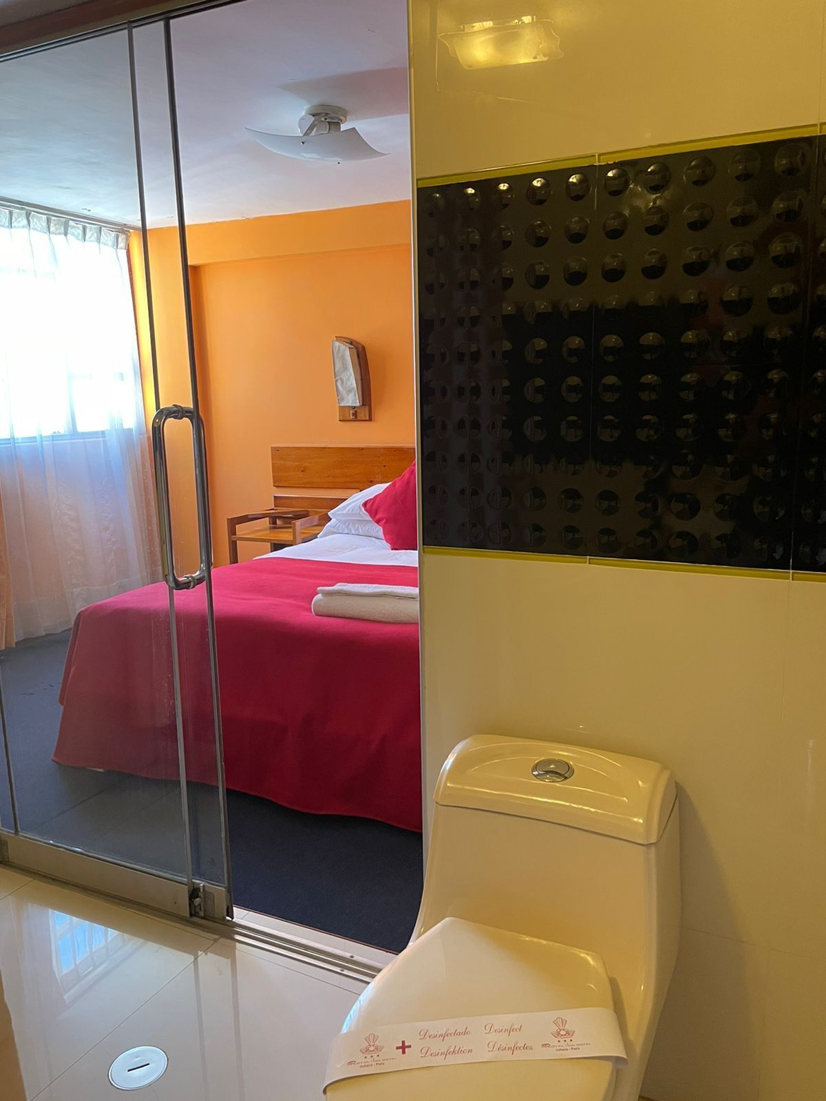 Una habitación de hotel con cama, mesita de noche, espejo, inodoro y pared con diseños circulares.