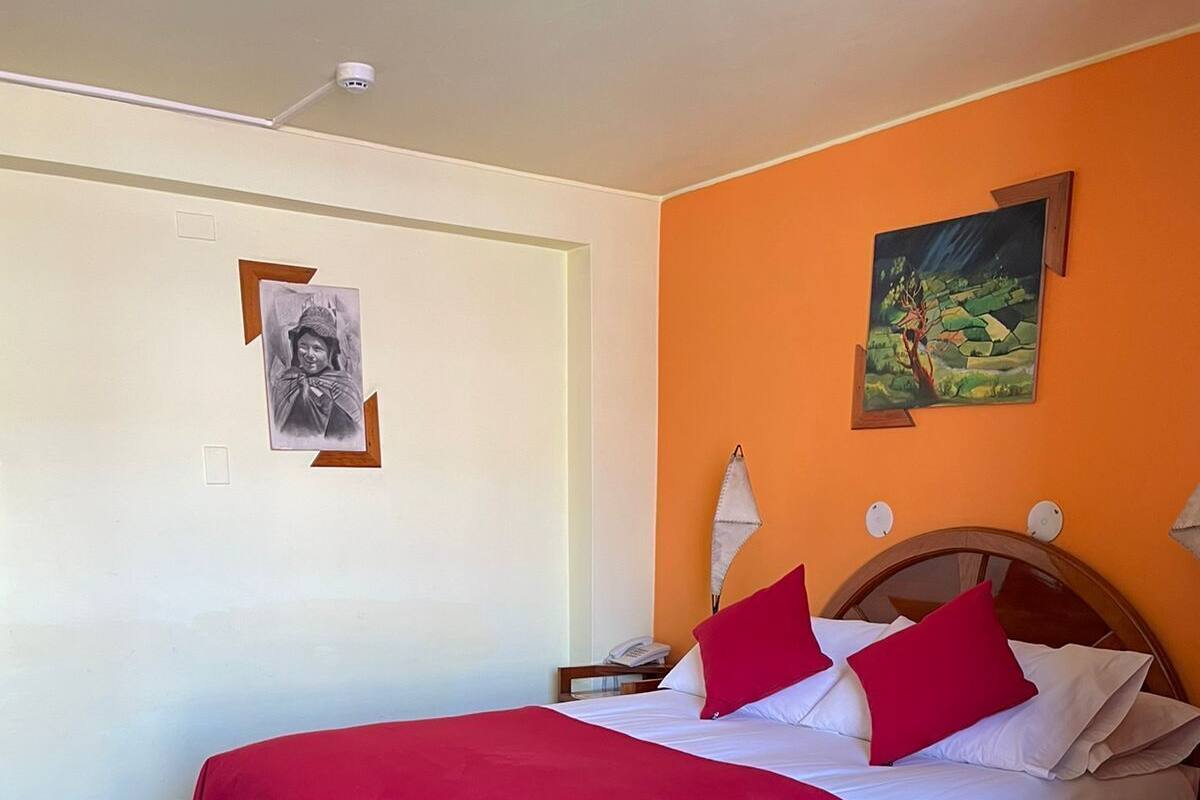 A hotel room with a bed, a nightstand, a painting, and a security camera on the ceiling.