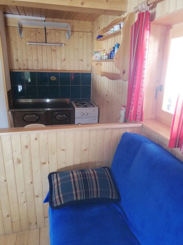A wooden interior with a kitchenette, a blue sofa, and a window with curtains.