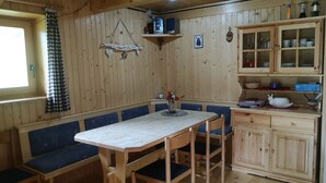 Un intérieur en bois comprenant une table à manger, des bancs et un coin cuisine avec des placards et des étagères.