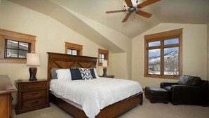 A bedroom with a large bed, wooden headboard, two bedside tables with lamps, a chair, and a large window with a view of a snowy landscape. - Majestic Mountain Family Escape - 4 bedroom/4Bathroom with lots of room and easy access to the slopes, river and town (Steamboat Springs)