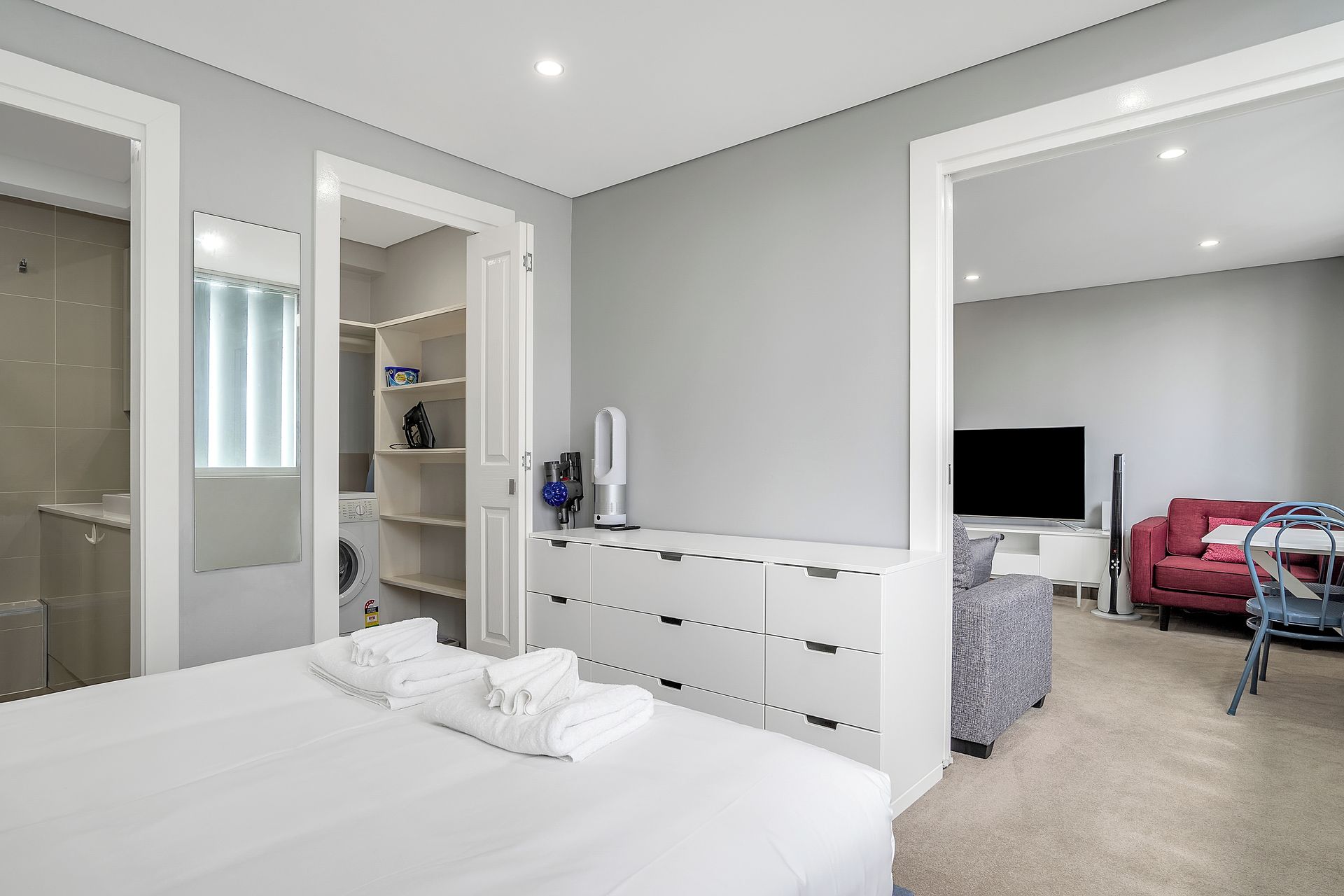 A modern bedroom with a large bed, a wardrobe, a TV, and a red sofa.