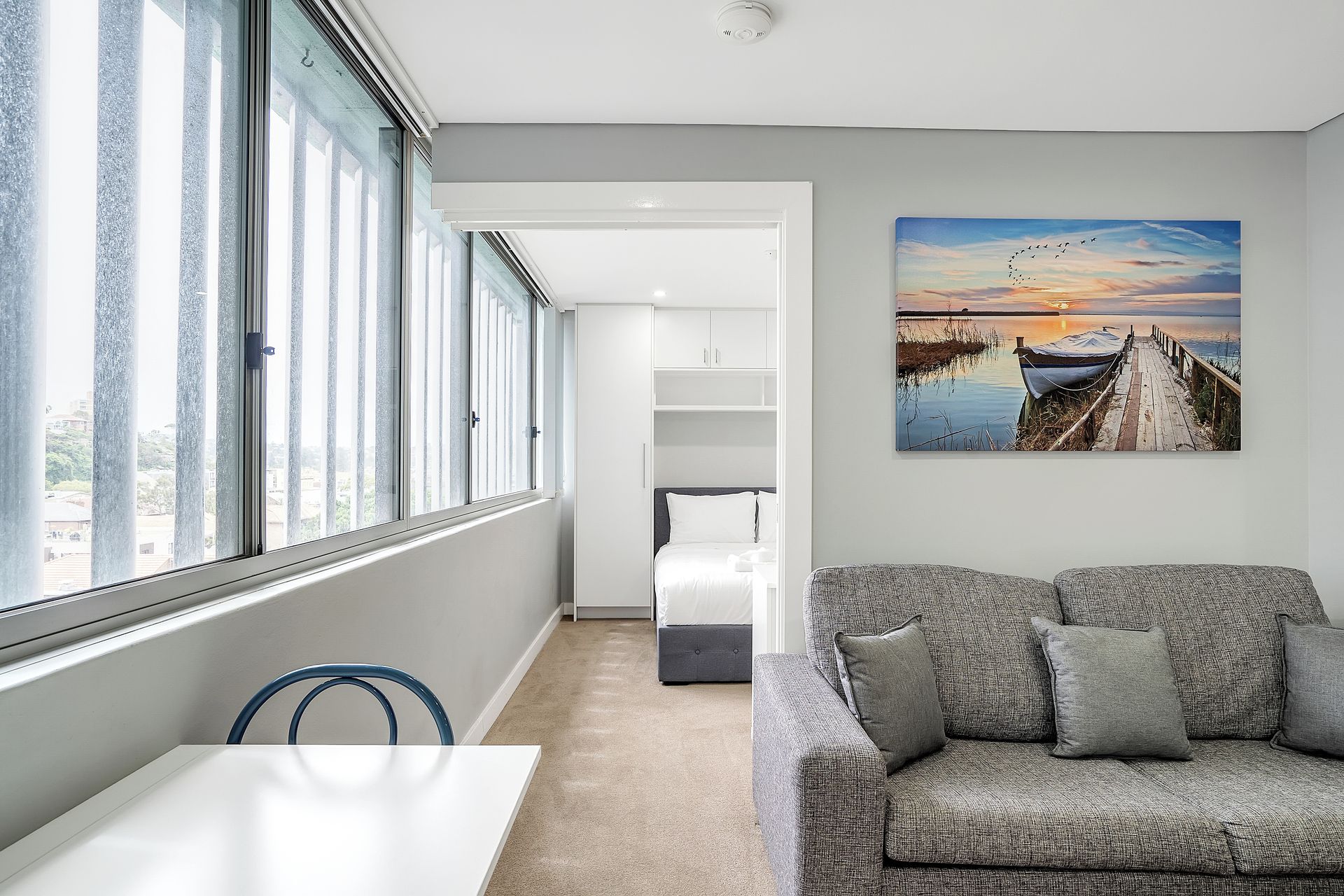 A modern room with a large window, a sofa, and a painting of a sunset over water.