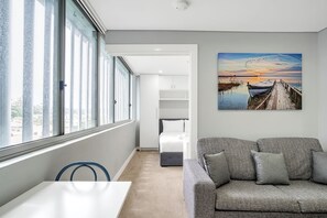 Une chambre moderne avec une grande fenêtre, un canapé et un tableau représentant un coucher de soleil sur l’eau.