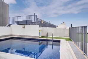 Une piscine sur le toit, avec une eau d’un bleu limpide, entourée d’une clôture métallique et d’un mur blanc.