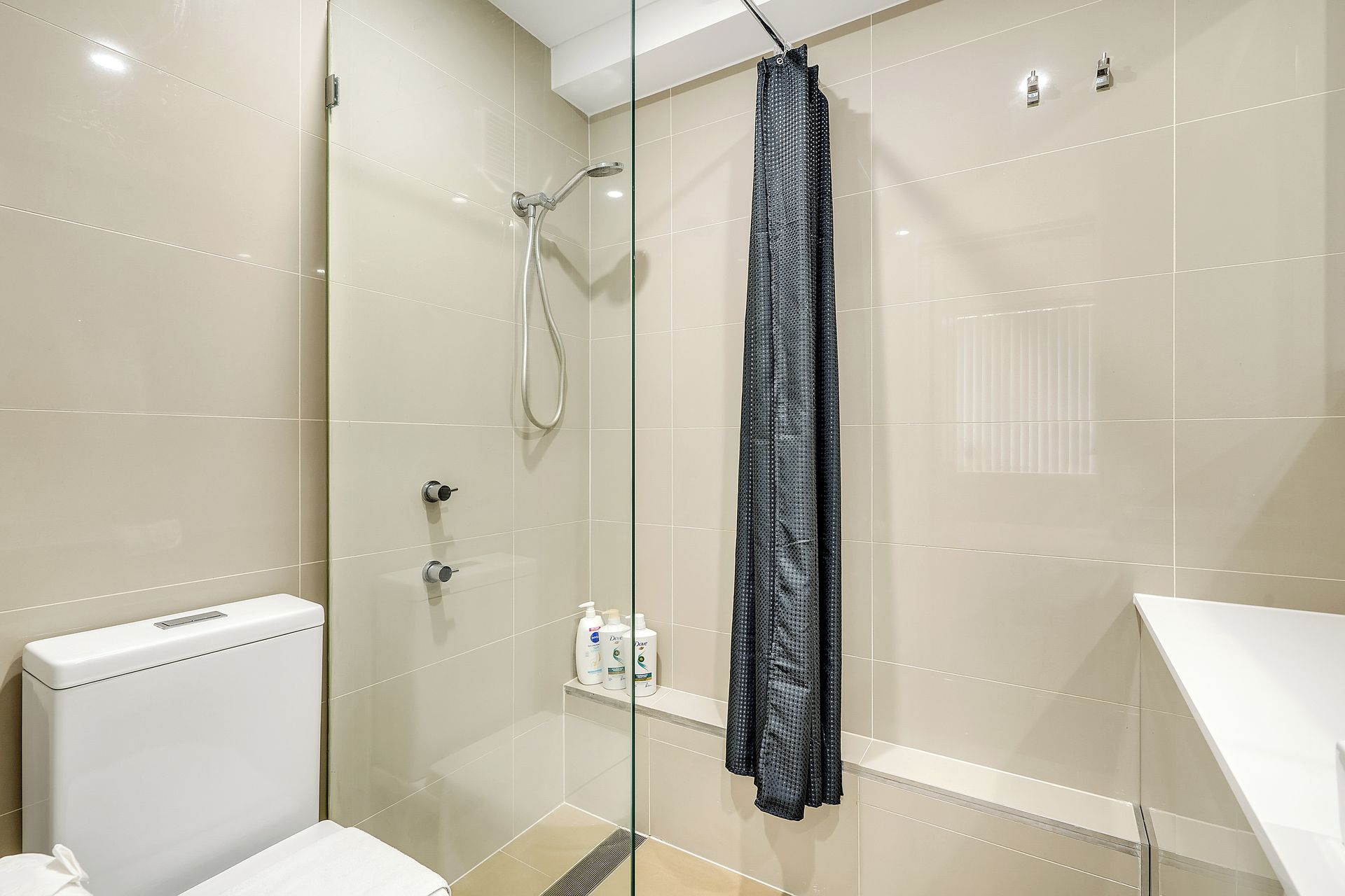 A modern bathroom with a glass-enclosed shower, a white toilet, and a shelf with toiletries.