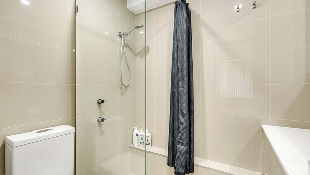 Et moderne badeværelse med en glasafskærmet brusekabine, et hvidt toilet og en hylde med toiletartikler.
