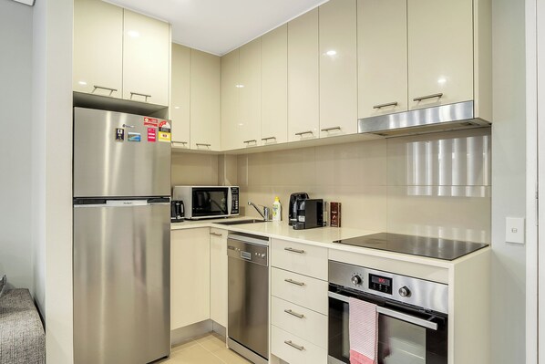 Cocina compacta con electrodomésticos de acero inoxidable, que incluyen un refrigerador, microondas y horno.
