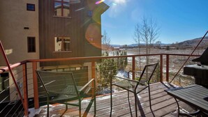 Eine Holzterrasse mit Metallstühlen und einem Grill, mit Blick auf eine verschneite Landschaft.