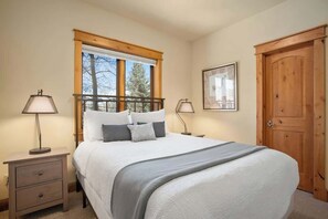 A bedroom with a bed, two bedside tables, a window with blinds, a door, and a framed picture on the wall. - Majestic Park - 4 Bed/4 Bathroom with Easy Ski  and Core Trail Access (Steamboat Springs)