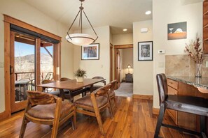 A dining area with a wooden table and chairs, a hanging light fixture, and a view through large windows. - Majestic Park - 4 Bed/4 Bathroom with Easy Ski  and Core Trail Access (Steamboat Springs)