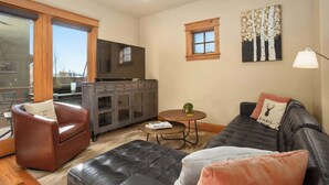 Ein Wohnzimmer mit einer Couch, einem Sessel, einem Couchtisch, einem Fernseher, einem Schrank und einem Fenster.