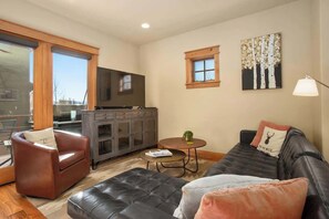 A living room with a sofa, a chair, a coffee table, a TV, a cabinet, and a window.