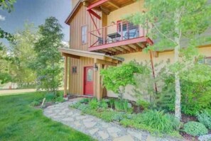 A two-story wooden house with a red door, a balcony, and a stone pathway leading to the entrance. - Majestic Park - 4 Bed/4 Bathroom with Easy Ski  and Core Trail Access (Steamboat Springs)