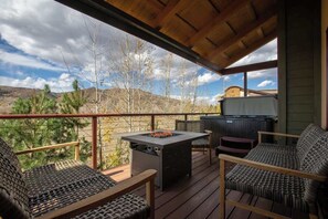 A covered outdoor deck with a fire pit, seating, and a view of the surrounding landscape. - Majestic Modern | 4BR, Private Hot Tub, Core Trail (Steamboat Springs)