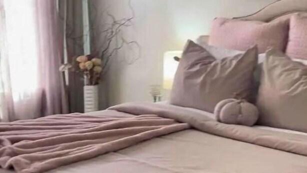 A neatly made bed with a pink blanket and pillows, a vase with dried flowers, and a painting on the wall. - PLG Boho Stay (Flatbush) (Brooklyn)