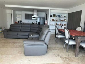 Ein modernes Wohnzimmer mit einer Eckcouch, einem Esstisch mit Stühlen und einer Küchenzeile im Hintergrund.