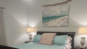 Ein Schlafzimmer mit einem Bett, zwei Nachttischen, einem Wandbild und einem Deckenventilator.