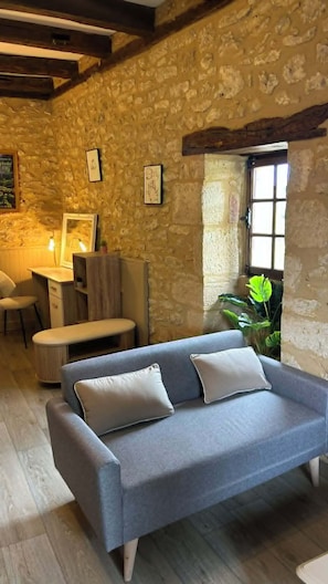 Une pièce avec un mur en pierre, un canapé bleu avec des coussins, un bureau en bois et une chaise.