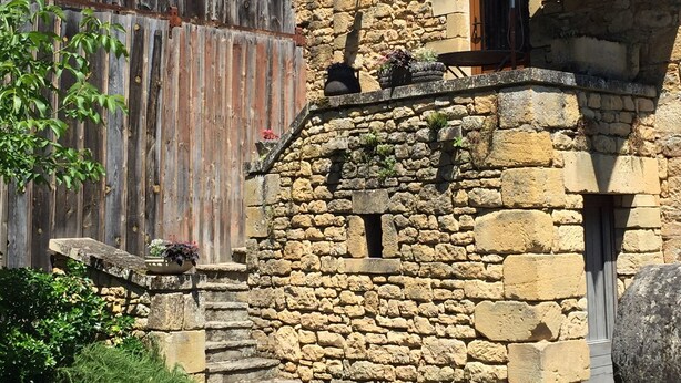 A rustic stone building with a wooden door and a small balcony with a table and potted plants. - "Le Pigeonnier", in the valley of the 5 castles in Périgord Noir (vezac)