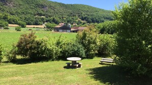 A patio area with a table and benches, surrounded by greenery and a view of a rural landscape with buildings and hills. - "Le Pigeonnier", in the valley of the 5 castles in Périgord Noir (vezac)