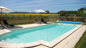 A rectangular swimming pool with a tiled edge, surrounded by a wooden fence. There are lounge chairs and umbrellas along the poolside. - "Le Pigeonnier", in the valley of the 5 castles in Périgord Noir (vezac)