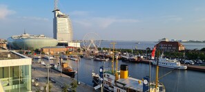 A marina with boats, a Ferris wheel, and modern buildings including a distinctive curved skyscraper. - Apartment 21—unobstructed 180° panoramic view from the apartment. Pure luxury. (Bremerhaven)