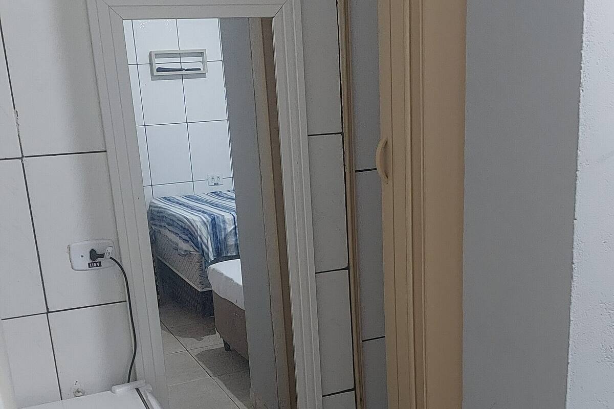 A small, narrow room with a bed, a chair, and a door leading to another room.
