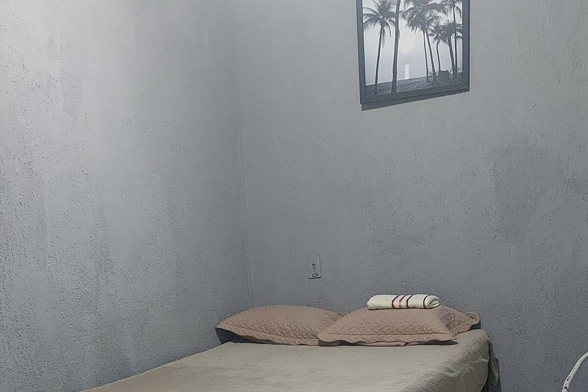 A small, dimly lit room with a single bed, a small table, and a wall-mounted picture.