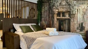 Een bed met wit beddengoed, twee groene kussens en een opgerolde handdoek.