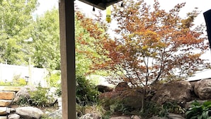Un bain à remous entouré de pierres, une terrasse en bois et, au fond, un arbre aux feuilles d’automne.
