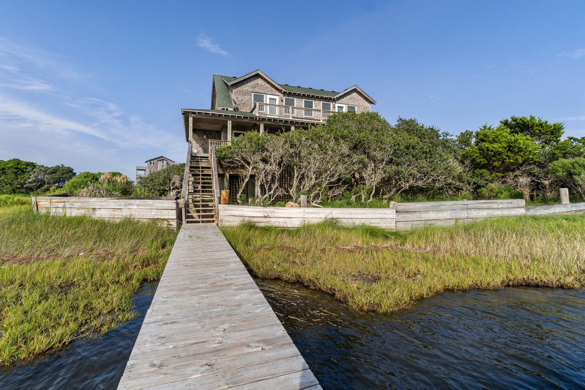 A wooden boardwalk leading to a large house with multiple levels and a staircase.