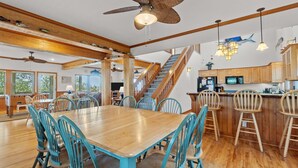 A spacious dining area with a wooden table and blue chairs, a kitchen with wooden cabinets, and a staircase leading to another level. - 7825-The Carolina Moon - Soundfront Frisco Home | Sunset Views (Frisco)