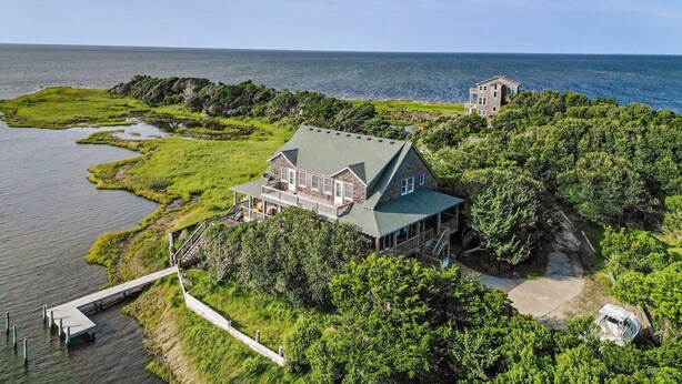 A large house with a green roof, surrounded by lush greenery and a dock extending into a body of water. - 7825-The Carolina Moon - Soundfront Frisco Home | Sunset Views (Frisco)