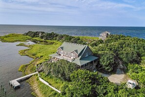 A large house with a green roof, surrounded by lush greenery and a dock extending into a body of water.