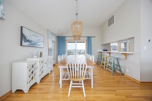 A dining area with a wooden table, white chairs, a hanging light fixture, and a view through the window.