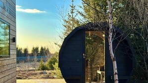 Una cabaña moderna con una fachada circular, una terraza de madera y vistas al bosque circundante.