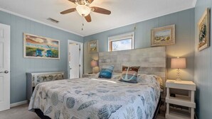 Un dormitorio con cama, ventilador de techo, mesita de noche y decoración en la pared.