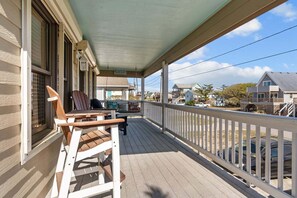 A covered porch with wooden chairs and a table, overlooking a residential area with houses and parked cars. - 5317-Labs & Crabs - Dog-Friendly KDH Retreat w/ Hot Tub & Yard (Kill Devil Hills)