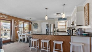 Una cocina con una isla de madera, taburetes de bar blancos, un reloj y un letrero que dice 'Stay Awake'.