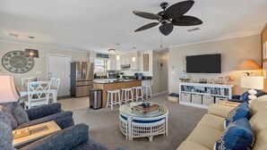 Una sala moderna con sofá, una mesa de centro, comedor con sillas, cocina con refrigerador y microondas, y un ventilador de techo.