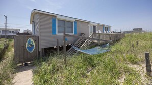Una casa davant de la platja amb terrassa de fusta, un hamaca i una barca petita a cobert.