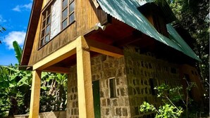Una cabaña rústica con base de piedra y estructura de madera, con techo de metal y un pequeño porche.