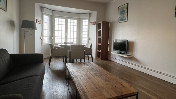 Un salon spacieux avec une table basse en bois, un canapé, une table à manger avec des chaises, un téléviseur et une grande fenêtre laissant entrer la lumière naturelle.
