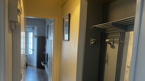 Un couloir étroit doté d’un plancher en bois, d’un luminaire, d’un miroir et d’une porte donnant sur une autre pièce.