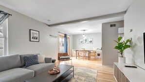 En moderne stue med en grå sofa, et sofabord og et spiseområde med træstole og et bord.