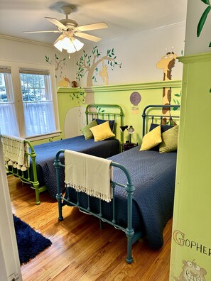 Une pièce avec deux lits en métal verts, un ventilateur de plafond et une fenêtre avec des rideaux.