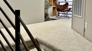 A staircase with a handrail leading to a room with a stone wall, a brown leather chair, and a white ceiling with recessed lighting.