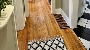 A hallway with wooden flooring, a patterned rug, and a door leading to a room with a blue chair and a radiator.