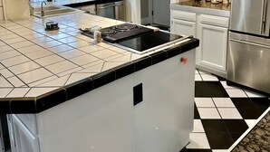 A modern kitchen with white cabinets, a black and white tiled floor, a stainless steel refrigerator, and a built-in island with a stovetop.